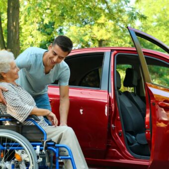 Conducteur accompagnateur de personnes à mobilité réduite qui aide une femme âgée à monter dans une voiture avec son fauteuil roulant