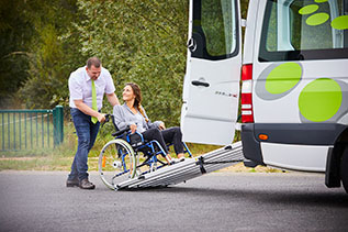 Homme aidant une femme à mobilité réduite à monter avec son fauteuil roulant dans un véhicule