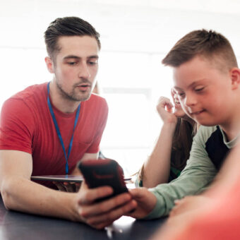 Educateur spécialisé qui montre son écran de téléphone à un enfant atteint de trisomie