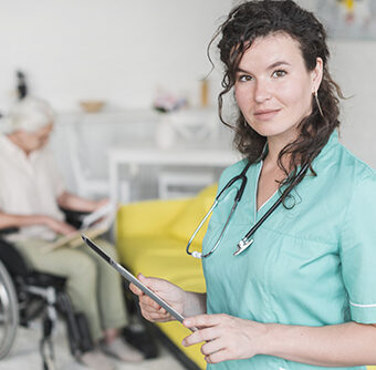 Portrait d'une infirmière libérale tenant une tablette numérique devant un patient âgé en fauteuil roulant