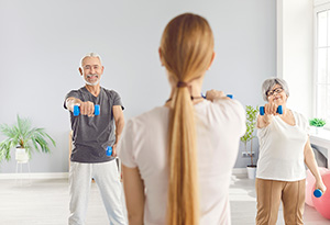 Animatrice en activité physique adaptée faisant une séance de sport avec un couple de seniors